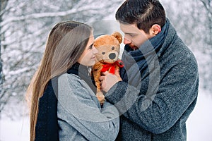 Handsome young man gives to his girlfriend a brown toy bear. Portrait of sweet couple hugging soft present looking cute