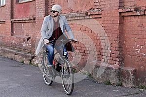 Handsome young man in grey coat and hat riding a bicycle street in the city