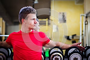 Handsome young man in gym sitting on dumbbells rack