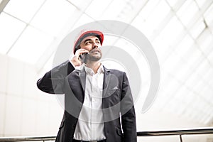 Handsome young man in hardhat holding blueprint and talking on the mobile phone while standing