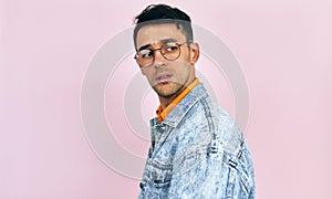 Handsome young man has uncertain exression on his face, isolated on pink studio background. Male wearing stylish casual clothes,