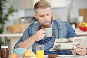 handsome young man having breakfast and reading newspaper at home
