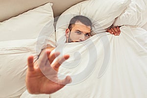 Handsome young man hiding under white blanket