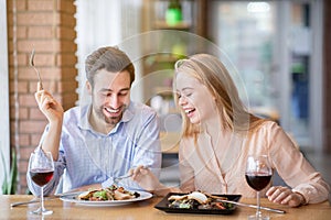 Handsome young man and his beloved woman having festive dinner with wine and yummy food at restaurant