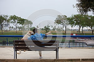 Handsome young man and his Labrador retriever dog sitting on a wooden bench in the park. The man and his pet are looking at the