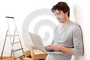 Handsome young man in his new flat using laptop