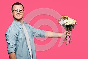 handsome young man holding bouquet of flowers and smiling at camera isolated