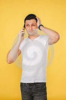 handsome young man holding a phone in his hand, talking emotionally on the phone on a yellow plain background