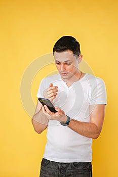 handsome young man holding a phone in his hand, talking emotionally on the phone on a yellow plain background