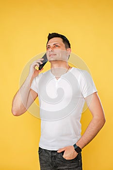 handsome young man holding a phone in his hand, talking emotionally on the phone on a yellow plain background