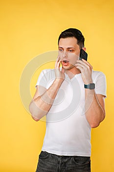 handsome young man holding a phone in his hand, talking emotionally on the phone on a yellow plain background