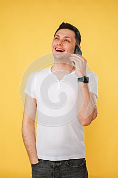 handsome young man holding a phone in his hand, talking emotionally on the phone on a yellow plain background