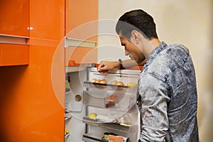 Handsome young man at home looking inside fridge