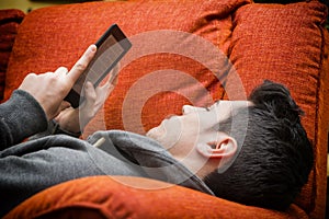 Handsome young man at home reading with ebook