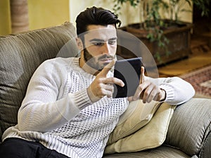 Handsome young man at home reading with ebook reader