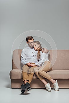 Handsome young man hugging beautiful girlfriend sleeping on his shoulder while sitting on sofa