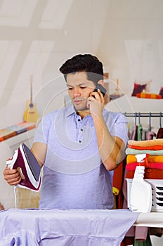Handsome young Man Ironing Clothes On Ironing Board while he is using his cellphone