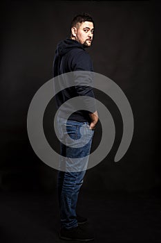 Handsome young man in jeans with a beard. Black background.