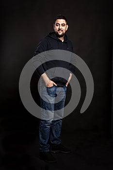 Handsome young man in jeans with a beard. Black background.