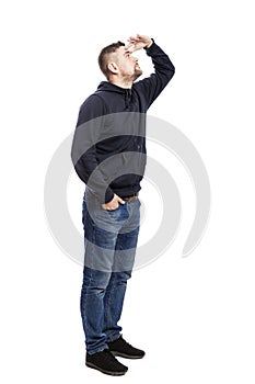 A handsome young man in jeans stands and looks into the distance. Hands in pockets. Side view. Isolated over white background.