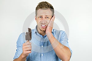 Handsome young man just bit piece of cold chololate ice-cream and suffers toothache on isolated white background