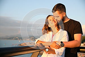 Handsome young man kissing his beautiful girlfriend on sea embankment