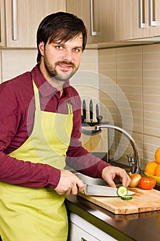Handsome young man in the kitchen with apron cutting vegetables