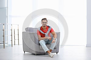 Handsome young man with laptop in armchair indoors