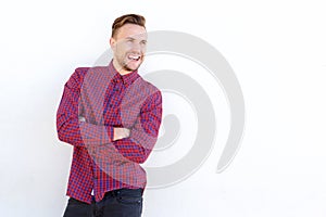 Handsome young man laughing with arms crossed against white wall