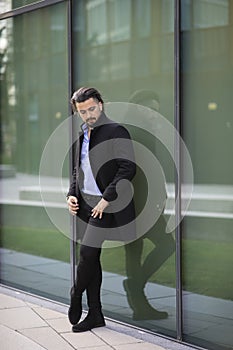 Handsome young man leaning against a glass fassade