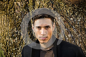 Handsome young man leaning against tree