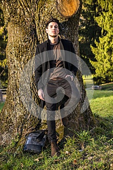 Handsome young man leaning against tree