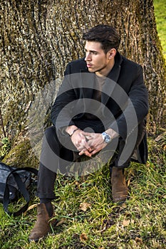 Handsome young man leaning against tree