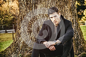 Handsome young man leaning against tree