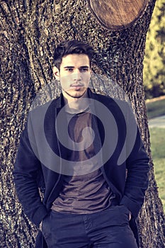 Handsome young man leaning against tree