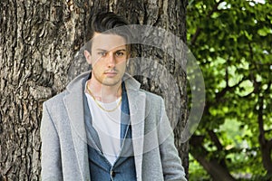 Handsome young man leaning against tree