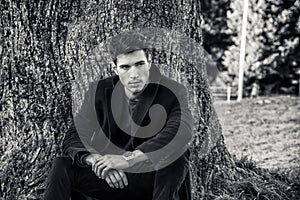 Handsome young man leaning against tree