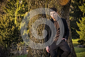 Handsome young man leaning against tree wearing coat