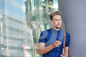 Handsome young man leaning against wall outside with cellphone