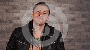 Handsome young man in leather jacket on naked body with tattoo on chest smiling and stroking hair. Portrait of brutal