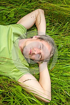 A handsome young man lies on green grass.