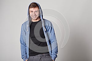 Handsome young man with light beard in blue hoodie, on gray bac