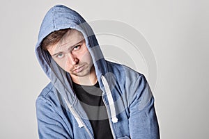 Handsome young man with light beard in blue hoodie, on gray bac