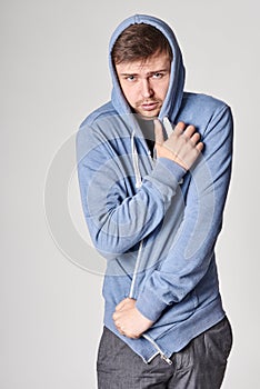 Handsome young man with light beard in blue hoodie, on gray bac