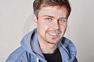 Handsome young man with light beard in blue hoodie, on gray bac