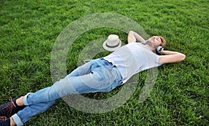 Handsome young man listening to music on green grass in park