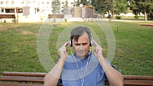 Handsome young man listening to music from his smartphone with headphones, dancing outside in the park on a bench in the