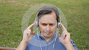 Handsome young man listening to music from his smartphone with headphones, dancing outside in the park on a bench in the
