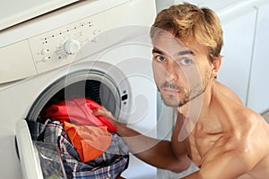 Handsome young man loads the laundry into the washing machine. Male housewife, bachelor concept