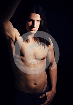 Handsome young man with long hair naked torso on black background